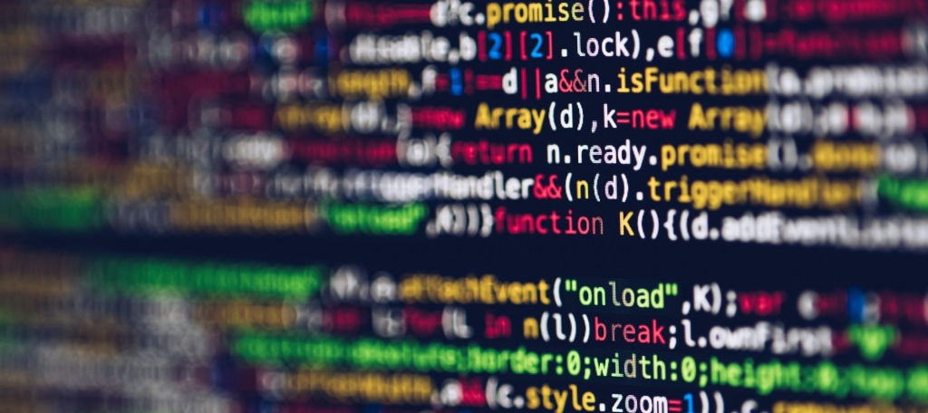 Zbliżenie ekranu komputera wyświetlającego kolorowe linie kodu programowania z podświetleniem składni w kolorze czerwonym, niebieskim, zielonym, żółtym i białym na ciemnym tle. Kod jest lekko rozmyty na krawędziach.